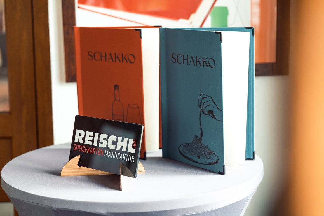 Zwei individuell gestaltete Speisekarten auf einem Präsentationstisch im Schauraum der Reischl Speisekarten Manufaktur.