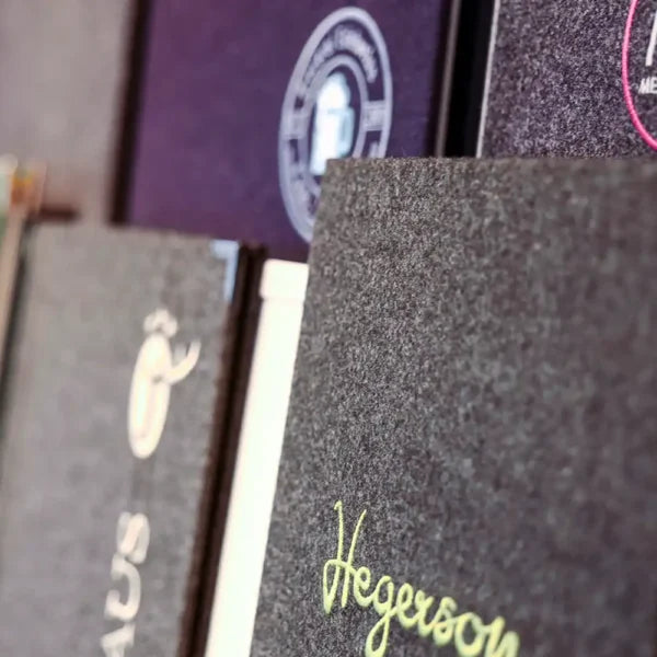 Detailaufnahme von Speisekarten aus Loden in verschiedenen Farben mit Veredelungen auf den Vorderseiten