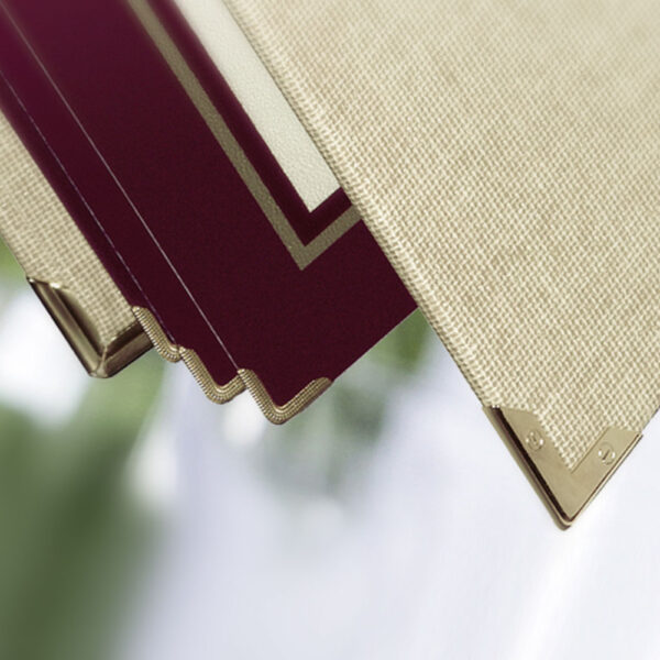 Detailaufnahme einer Speisekarte aus Buchleinen in der Farbe Natur und Weinrot mit goldenen Metallecken