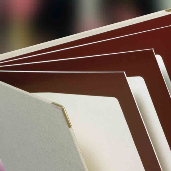 Detailaufnahme einer Speisekarte Librette aus Buchleinen in der Farbe grau mit Metallecken aus Gold und Transette-Hüllen in der Farbe Weinrot