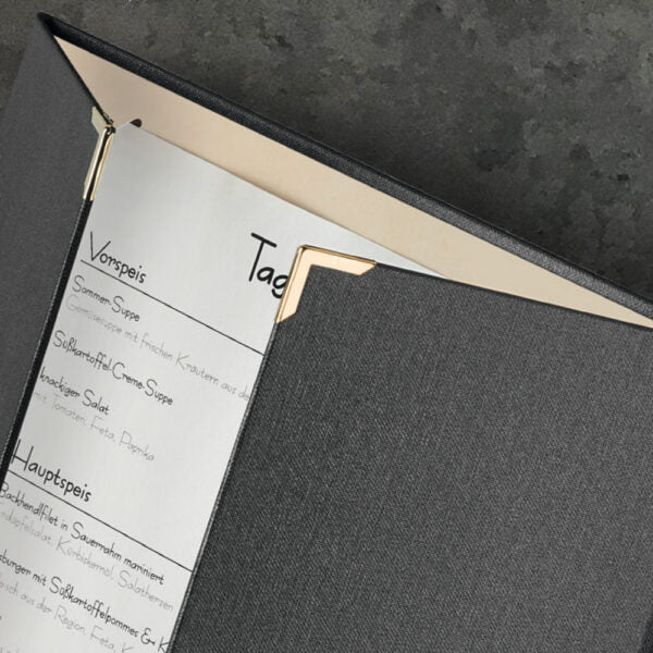 Detailaufnahme einer halb geöffneten Speisekarte Ouvertüre aus Buchleinen in der Farbe Lava mit Metallecken in Gold