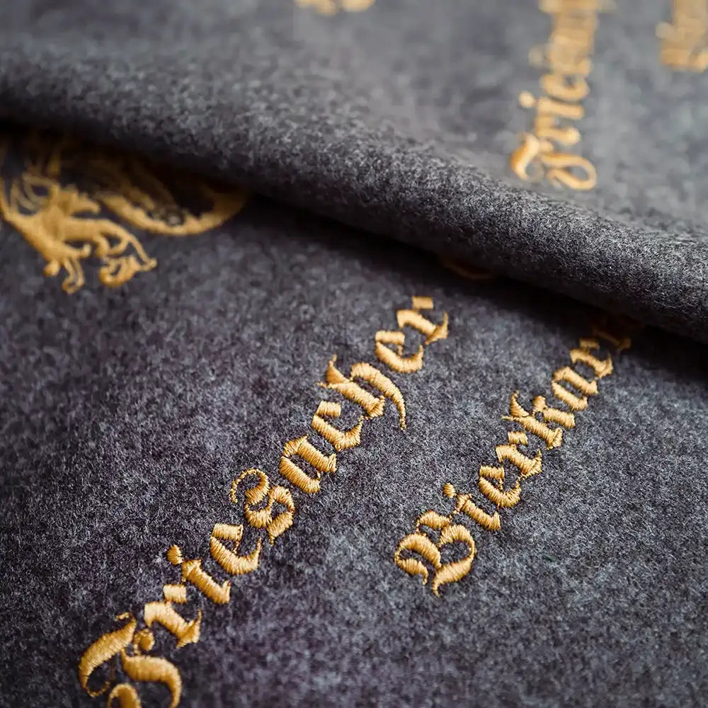 Detailaufnahme des Materials Loden in der Farbe grau mit goldener Stickerei