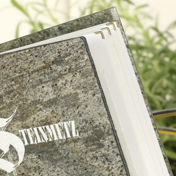 Detailaufnahme einer Speisekarte aus Stein mit Metallecken in der Farbe Gold und weißem UV-Druck auf der Vorderseite